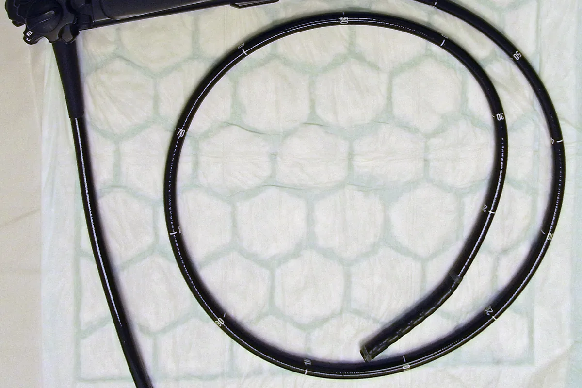 A flexible colonoscope, a long black tube with a camera at its tip, coiled on a table